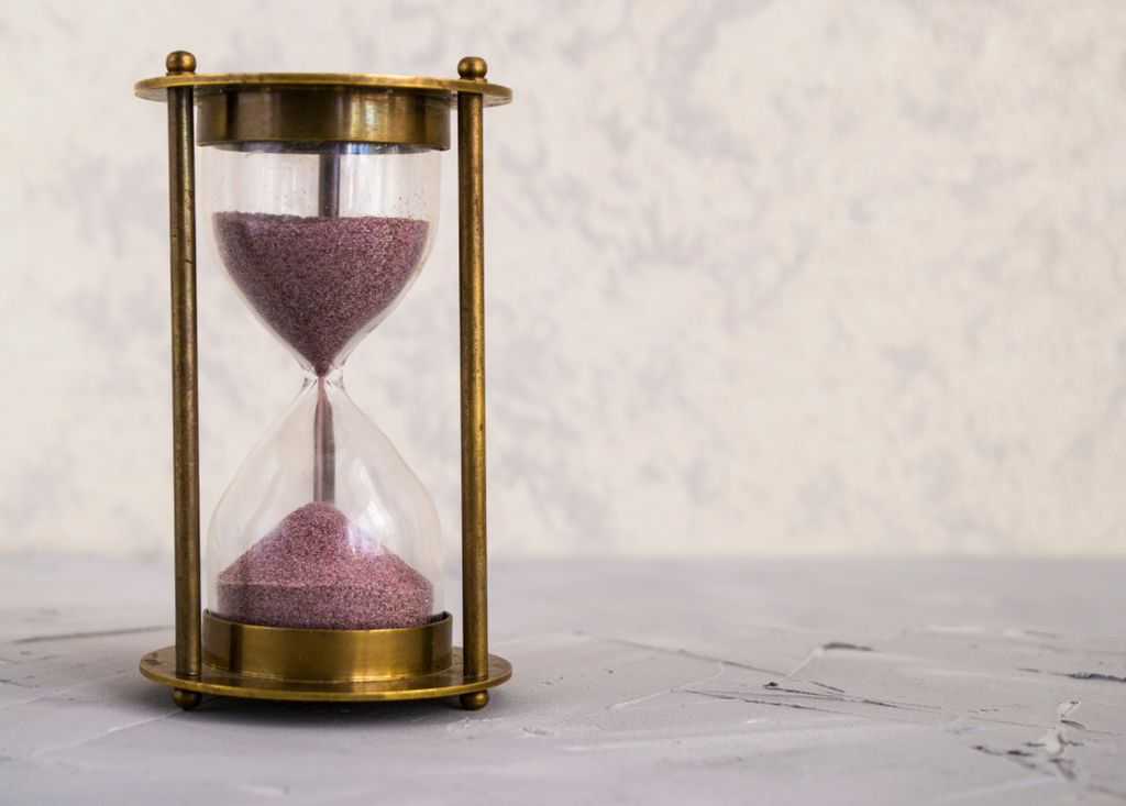 A traditional hourglass with pink sand, symbolizing time and patience on a textured surface.